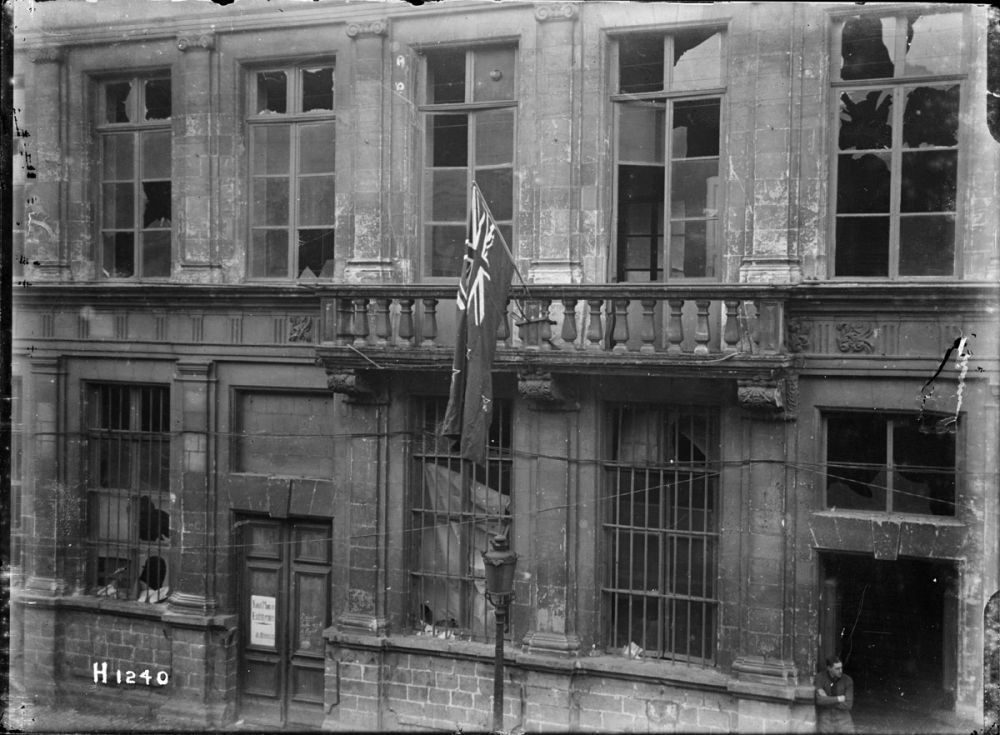A New Zealand flag, presented to the town of Le Quesnoy, hangs over the damaged town hall. November 1918.